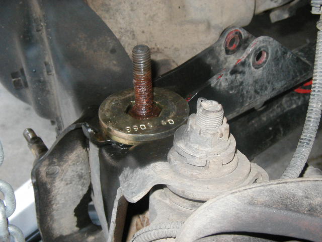 Rusty threaded bolt through stamped washer near greasy ball joint on undercarriage