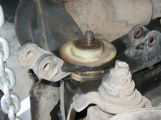 Underside suspension mount with threaded stud, rusty isolator bushing, and chain nearby