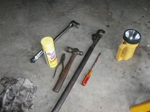 1995 Ford Bronco - A collection of tools, including a hammer, wrenches, pliers, a screwdriver, a spray can, and a flashlight, are arranged on a concrete surfa…