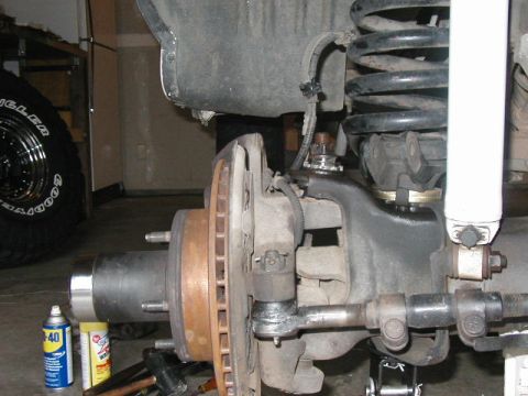 1995 Ford Bronco - Close-up of a vehicle's front suspension system, including the brake rotor and tie rod assembly. A can of WD-40 is on the floor.