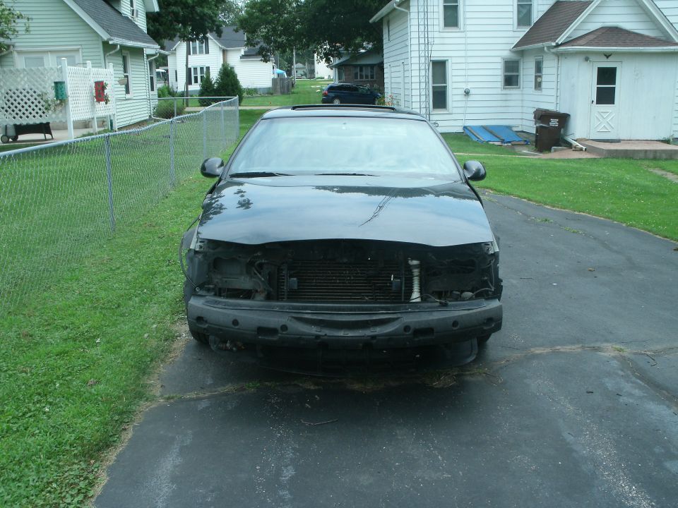 Front view of black car missing bumper and grille. Supermotors.net logo visible