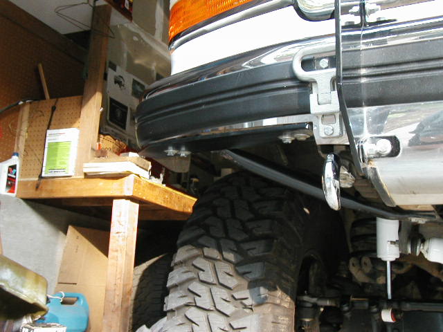 Front corner of dark SUV showing bumper, chrome, and large mud tire in a garage.