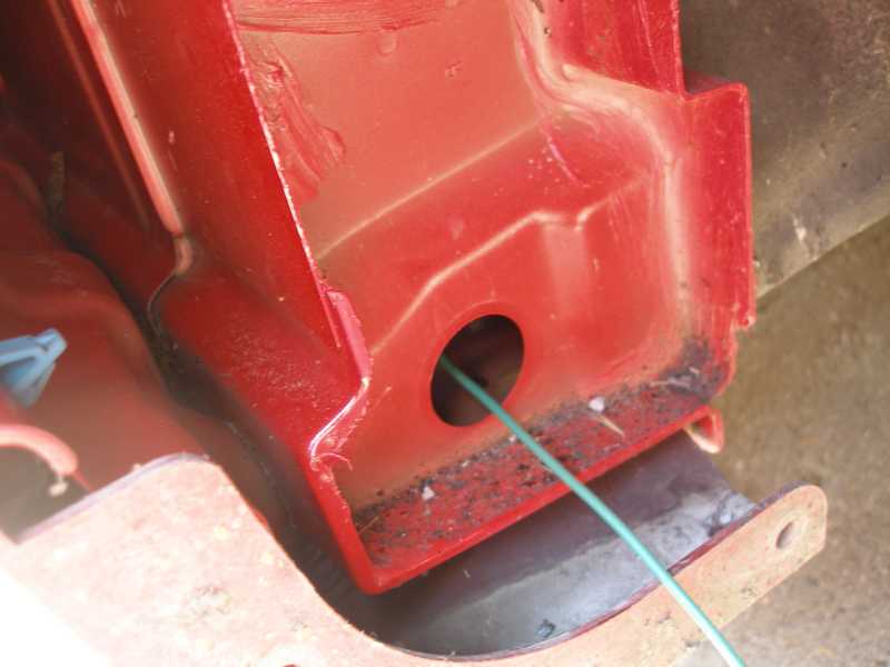 Close-up of red painted metal structure with a hole and a green wire passing through it
