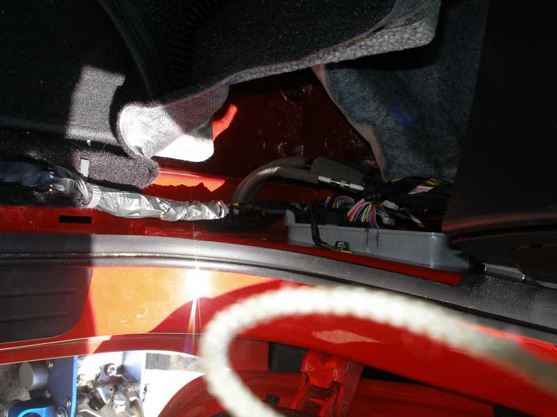 Door sill with carpet pulled back exposing wiring harness and connector block on red floor pan