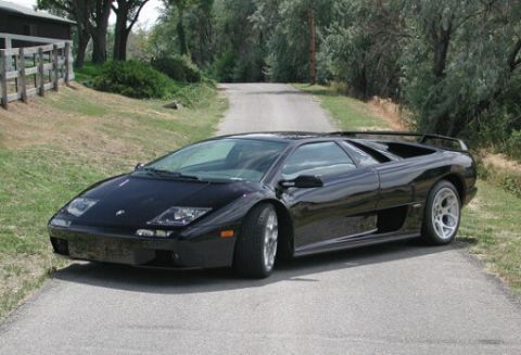 1998 Ford Crown Victoria - Black Lamborghini Diablo sports car on a paved driveway surrounded by trees.