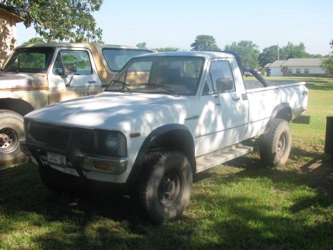 1985 Ford Bronco - White pickup truck parked in a grassy area next to another vehicle.