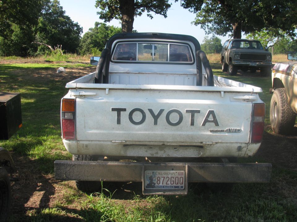 White Toyota pickup truck rear view, with roll bar, dirty bumper, and license plate 872GOQ