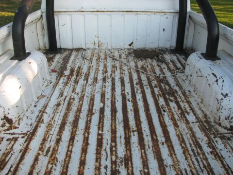 1985 Ford Bronco - The interior of a white truck bed shows a rusty floor and black roll bar, with a "Supermotors.net" watermark.