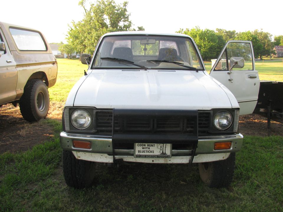 White pickup truck with open driver's door, parked on grass next to a tan SUV