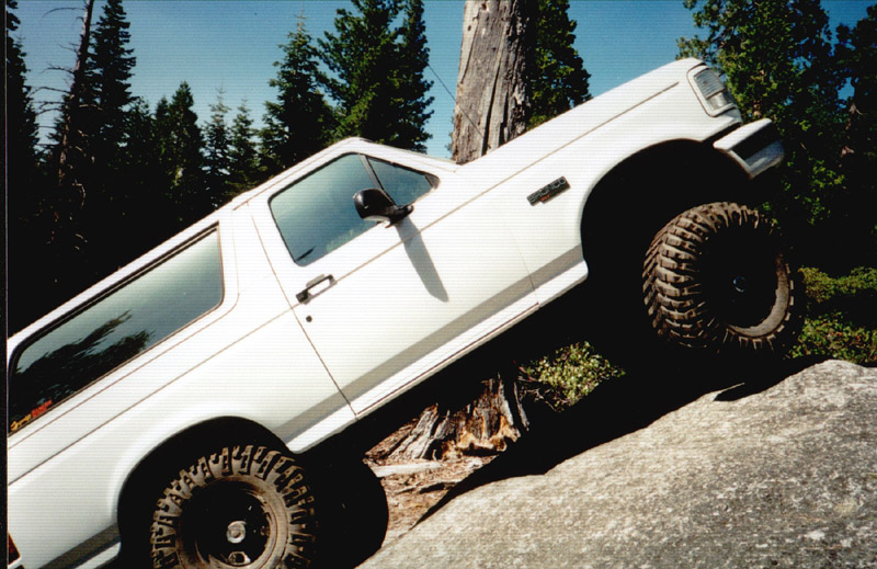 White lifted Ford Bronco climbing a steep granite rock slab on a pine mountain trail