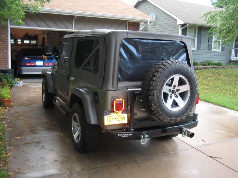 2005 Jeep Wrangler - Rear view of a 2005 Jeep Wrangler parked in a driveway, with a blue car visible in the garage.