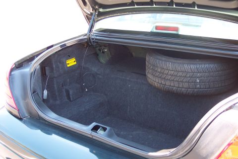 2001 Ford Crown Victoria - Trunk interior of a sedan, including the spare tire and carpeting. A yellow warning sticker is present.