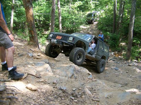 1992 Jeep YJ - Two Jeeps navigate a challenging off-road trail through a wooded area.