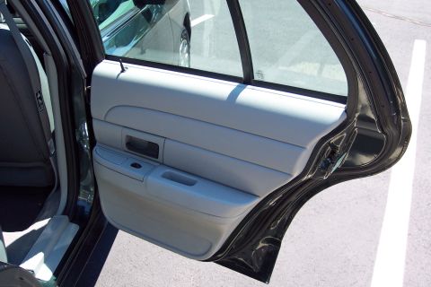2001 Ford Crown Victoria - The interior of a dark green sedan is visible with the rear passenger door open, revealing the door panel and seat.