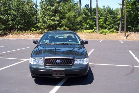 2001 Ford Crown Victoria - A dark green Ford Crown Victoria is parked in an empty lot with trees in the background.