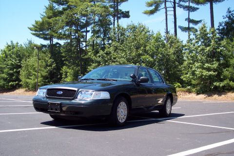 2001 Ford Crown Victoria - A dark green 2001 Ford Crown Victoria sedan is parked in an empty lot on a sunny day.