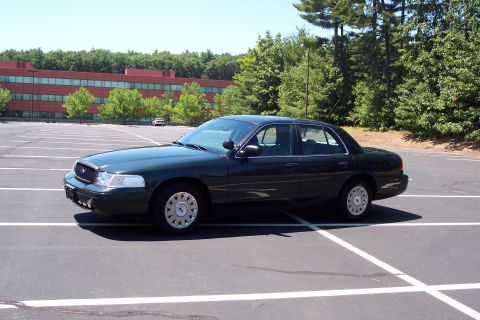 2001 Ford Crown Victoria - This sedan is parked in a large, empty lot with a red brick building in the background.