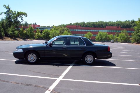 2001 Ford Crown Victoria - A dark sedan is parked in a lot with a modern building in the background.