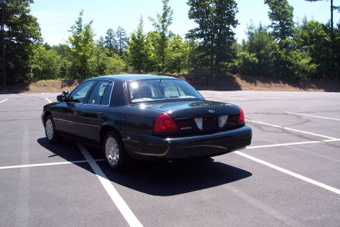 2001 Ford Crown Victoria - A dark green sedan is parked in a lot with trees in the background.