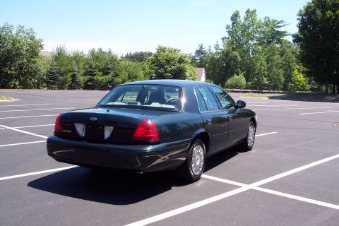 2001 Ford Crown Victoria - Rear 3/4 view of a dark green 2001 Ford Crown Victoria parked in an empty lot on a sunny day.