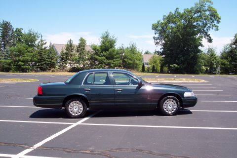 2001 Ford Crown Victoria - A dark green Ford Crown Victoria is parked in a lot on a sunny day.