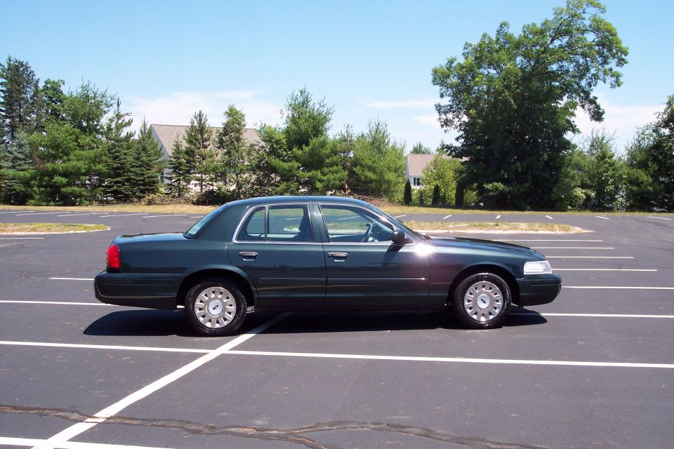 Dark green Ford Crown Victoria parked in an empty lot. Side view shows the car's profile