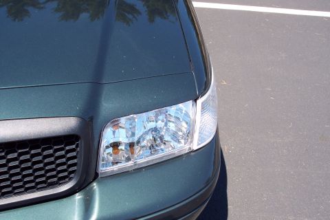 2001 Ford Crown Victoria - Close-up of the front corner of a dark green sedan, showing the headlight and grille detail.