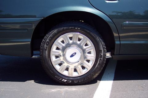 2001 Ford Crown Victoria - The rear wheel and fender of a dark green 2001 Ford Crown Victoria, a Ford logo on the hubcap.