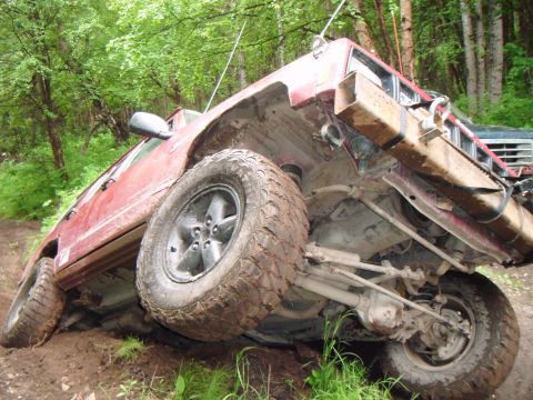1998 Jeep Cherokee - This red SUV is tilted precariously on a muddy trail, revealing its undercarriage and suspension system.