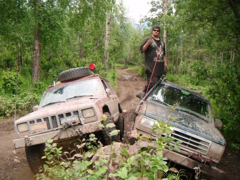1998 Jeep Cherokee - Two SUVs are stuck on a dirt trail surrounded by trees, with a person standing on one of them.