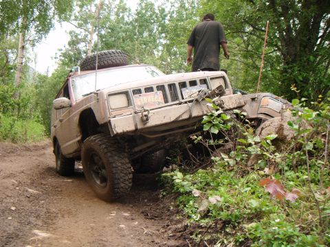 1998 Jeep Cherokee - A Jeep Cherokee navigates a muddy off-road trail, with another vehicle obscured by foliage.