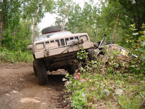 1998 Jeep Cherokee - A tan 1998 Jeep Cherokee navigates a challenging off-road trail, tilted precariously on a muddy embankment.