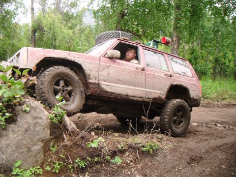 1998 Jeep Cherokee - A red Jeep Cherokee navigates a challenging off-road trail with a driver inside.