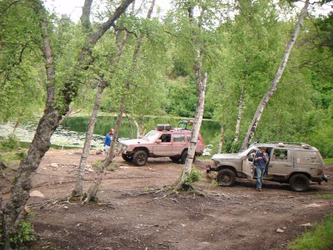 1998 Jeep Cherokee - Two SUVs are parked by a lake surrounded by trees.
