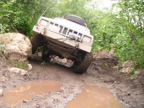 1998 Jeep Cherokee - A tan 1998 Jeep Cherokee tackles a challenging muddy and rocky off-road path, demonstrating its off-road capabilities.