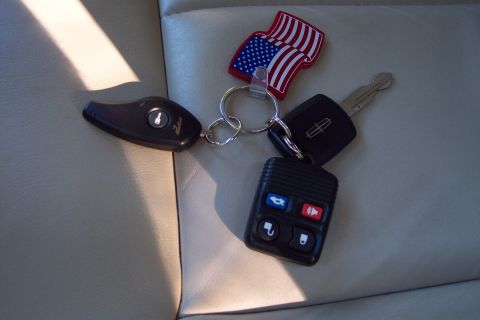 2001 Ford Crown Victoria - A set of car keys, including a Lincoln fob and an American flag charm, rests on a leather surface.