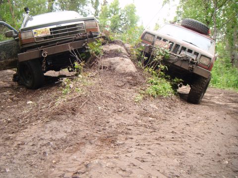 1998 Jeep Cherokee - Two off-road vehicles navigate a challenging muddy terrain, with one Jeep Cherokee angled precariously.