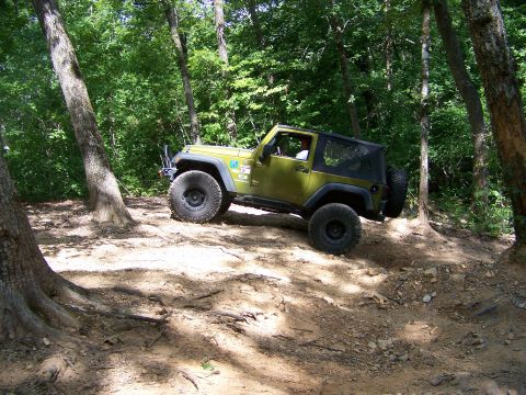 1992 Jeep YJ - Green Jeep Wrangler navigates a wooded trail with steep inclines and loose dirt.
