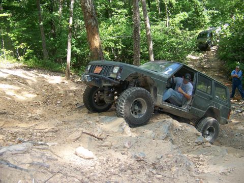 1992 Jeep YJ - A green 1992 Jeep Cherokee XJ navigates a rocky trail with another Jeep visible in the background.