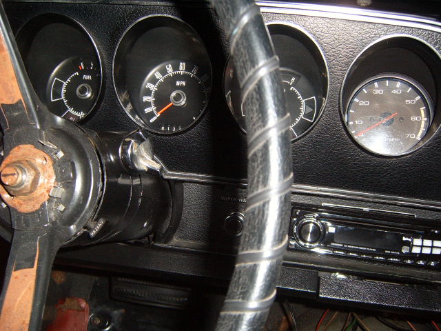 Close-up of a car's dashboard with fuel and speed gauges, a steering wheel, and a radio