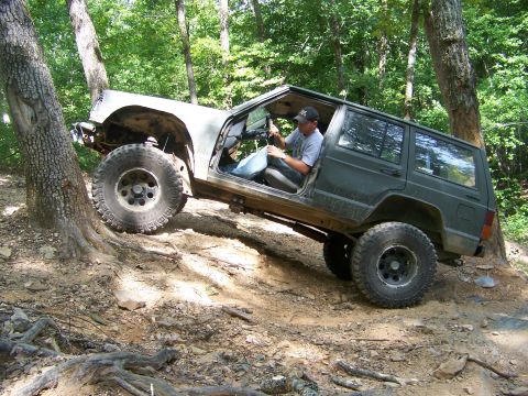 1992 Jeep YJ - A Jeep Cherokee XJ navigates a steep, wooded trail with its front fender missing.