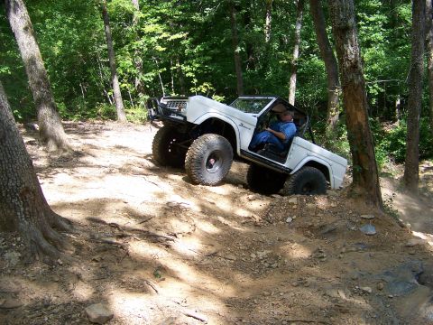 1992 Jeep YJ - This white off-road SUV navigates a steep, wooded trail, demonstrating its climbing capability.
