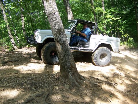 1992 Jeep YJ - Man drives a white off-road vehicle through a wooded area on a dirt path.