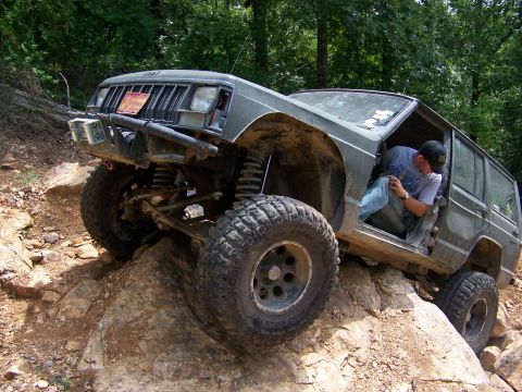 1992 Jeep YJ - A modified Jeep Cherokee XJ navigates a rocky off-road trail with its driver visible inside.