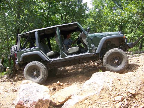 1992 Jeep YJ - A green Jeep Wrangler navigates a challenging rocky terrain with trees in the background.
