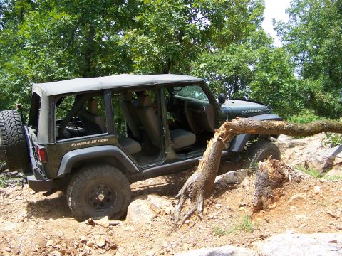 1992 Jeep YJ - A green Jeep Wrangler navigates a challenging off-road course, with a fallen tree obstructing its path.