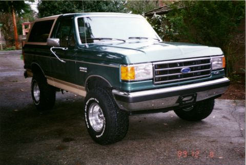 1990 Ford Bronco - 1990 Ford Bronco in green with tan side trim, seen from the front three-quarter view.