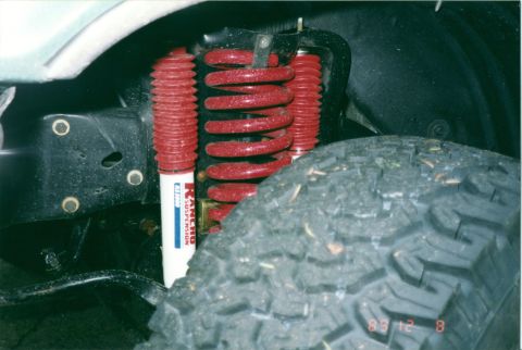 1990 Ford Bronco - Close-up of vehicle suspension components, including a Rancho shock and red coil spring.