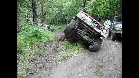 1998 Jeep Cherokee - An overturned Jeep Cherokee lies on its side on a dirt path in a wooded area, with another Jeep visible.