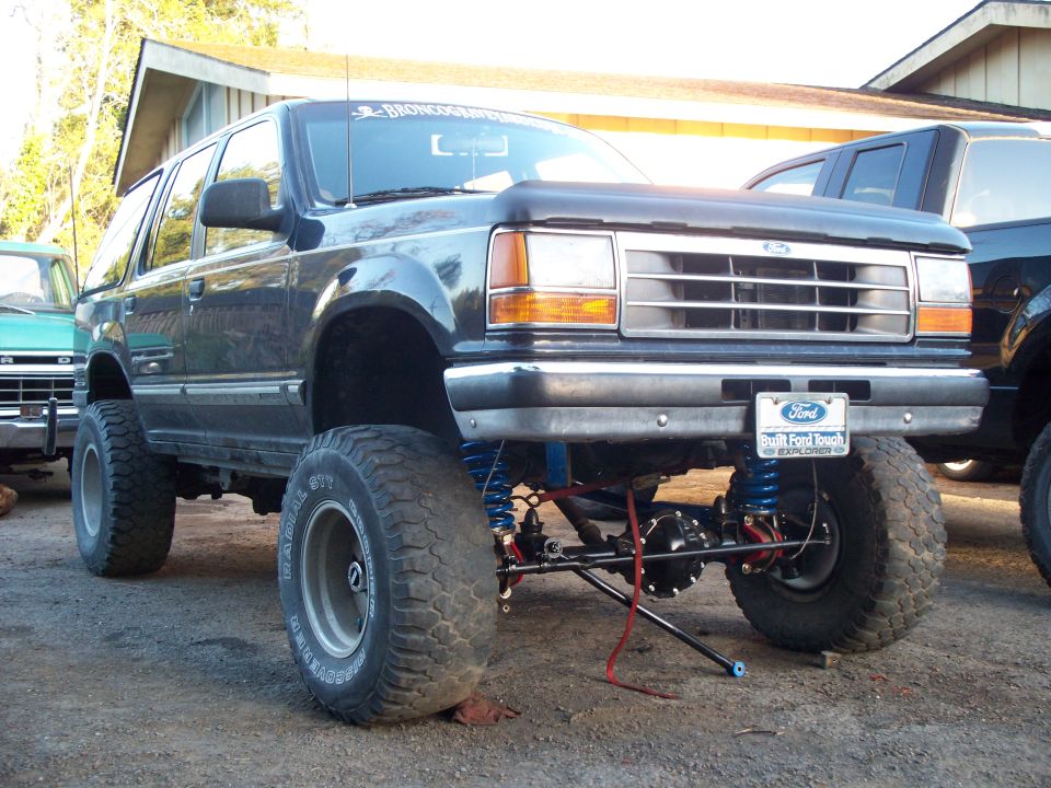 Lifted first-generation Ford Explorer with large tires and suspension modifications. Another vehicle is partially visible to the left